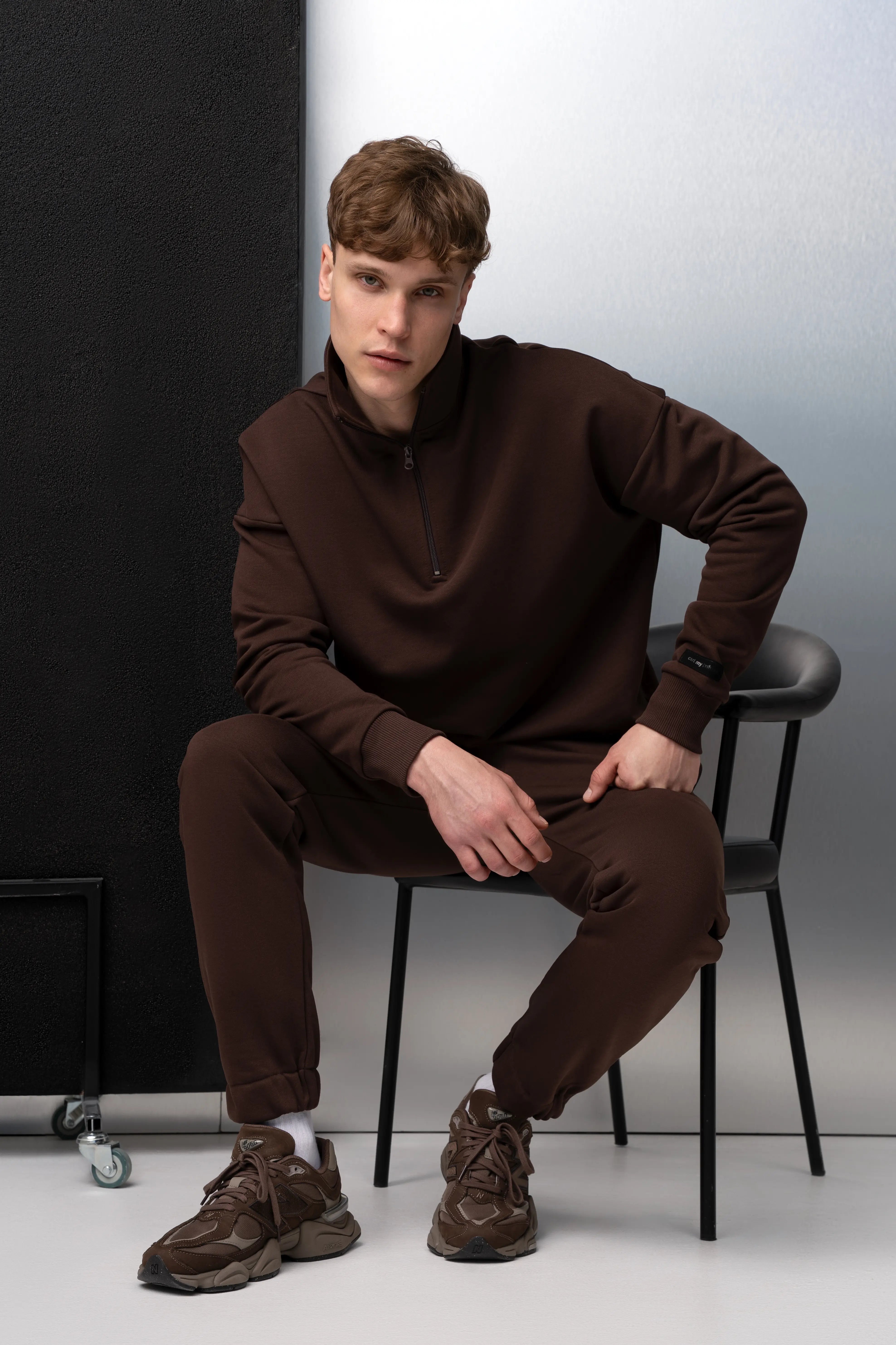 Der Mann sitzt in einem braunen Anzug aus flauschfreiem Stoff und einem Pullover mit hohem Kragen