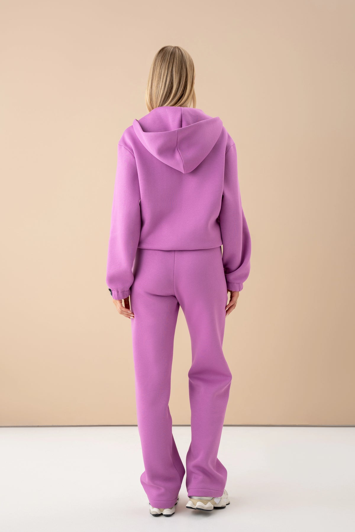 Das Model mit pastellrosa Pullover und Hose steht mit dem Rücken zur Kamera, Outfit von cutmyfashion im Studio