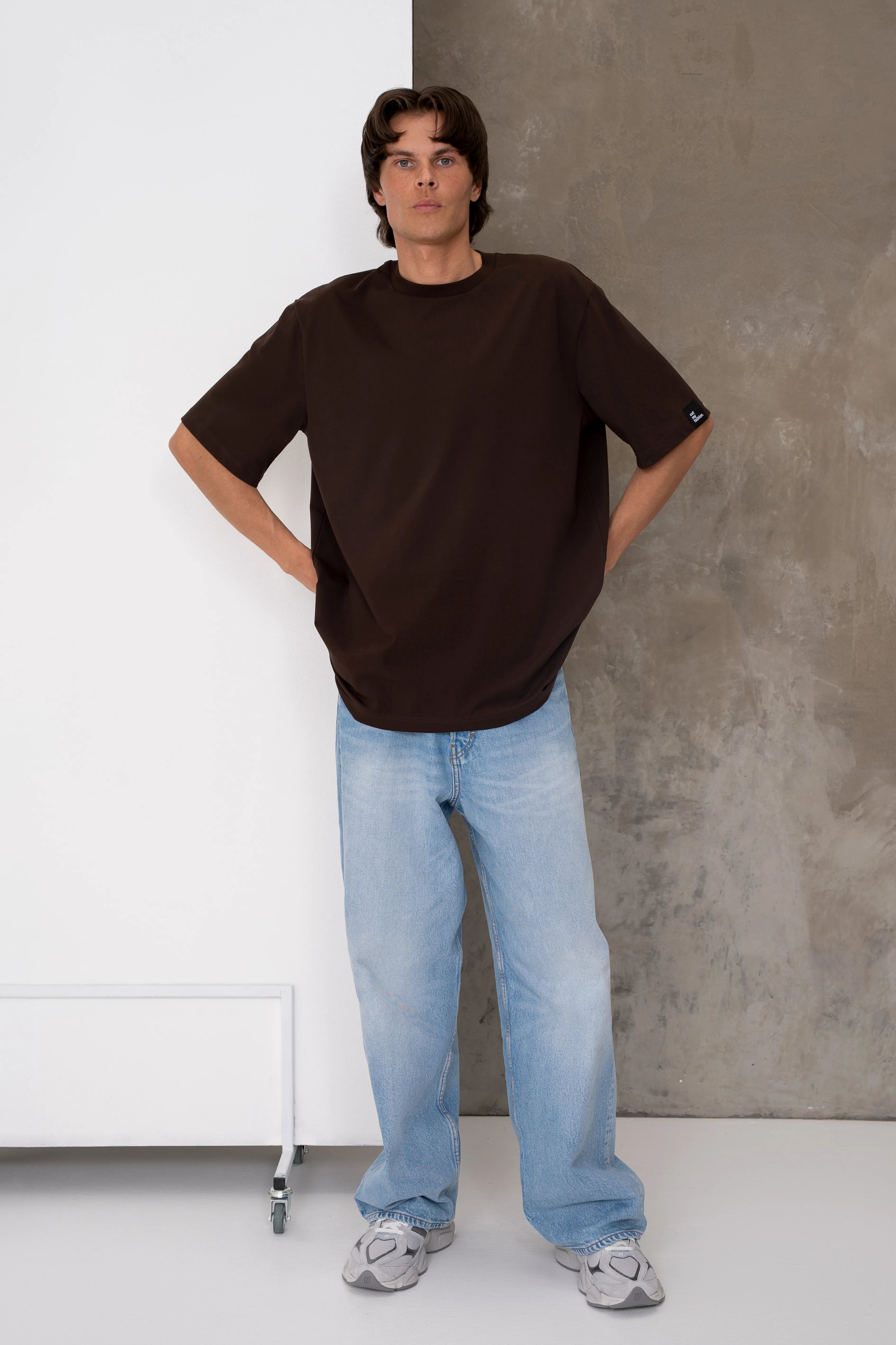 Rudi vyriški oversized marškinėliai trumpomis rankovėmis su apvalia kaklo iškirpte, nuleista pečių linija ir laisvu siluetu, derinami su šviesiais džinsais, pilnas vaizdas