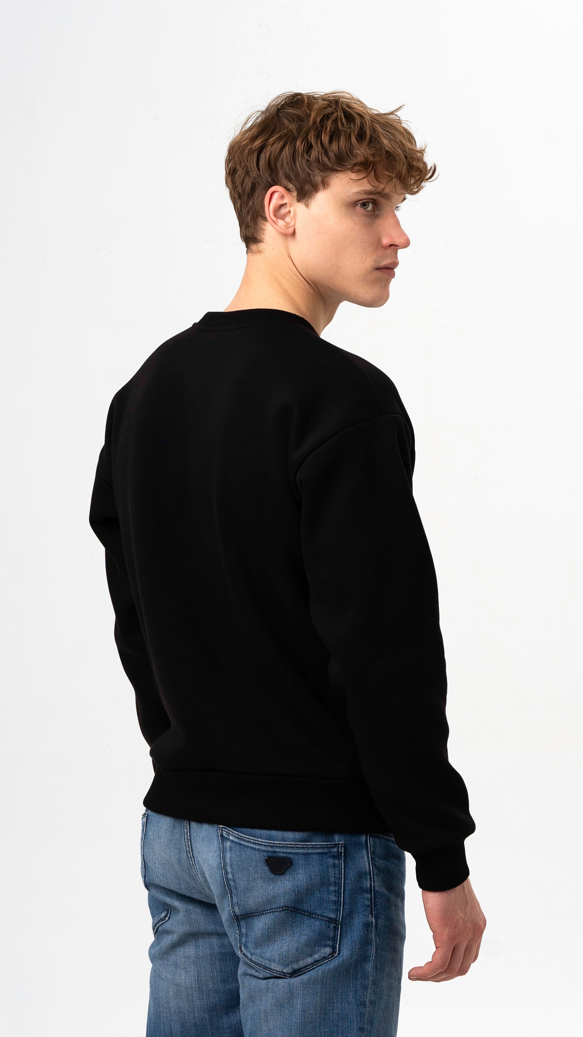 Vaikinas pozuoja ir dėvi juodos spalvos džemperį