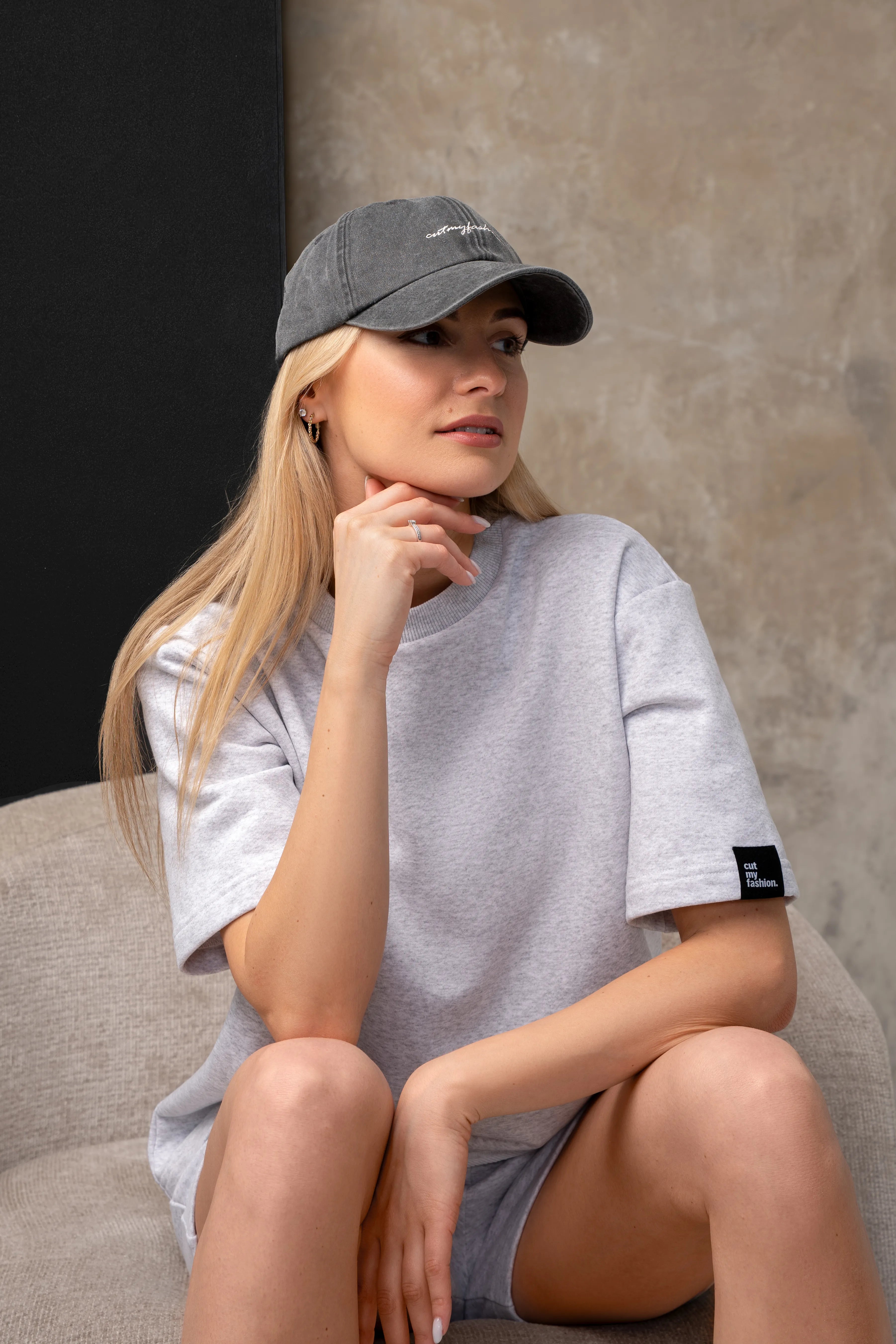 Ein Damenkostüm in Melange-Farben mit einer locker sitzenden Bluse und Shorts; das Model sitzt in einem Sessel