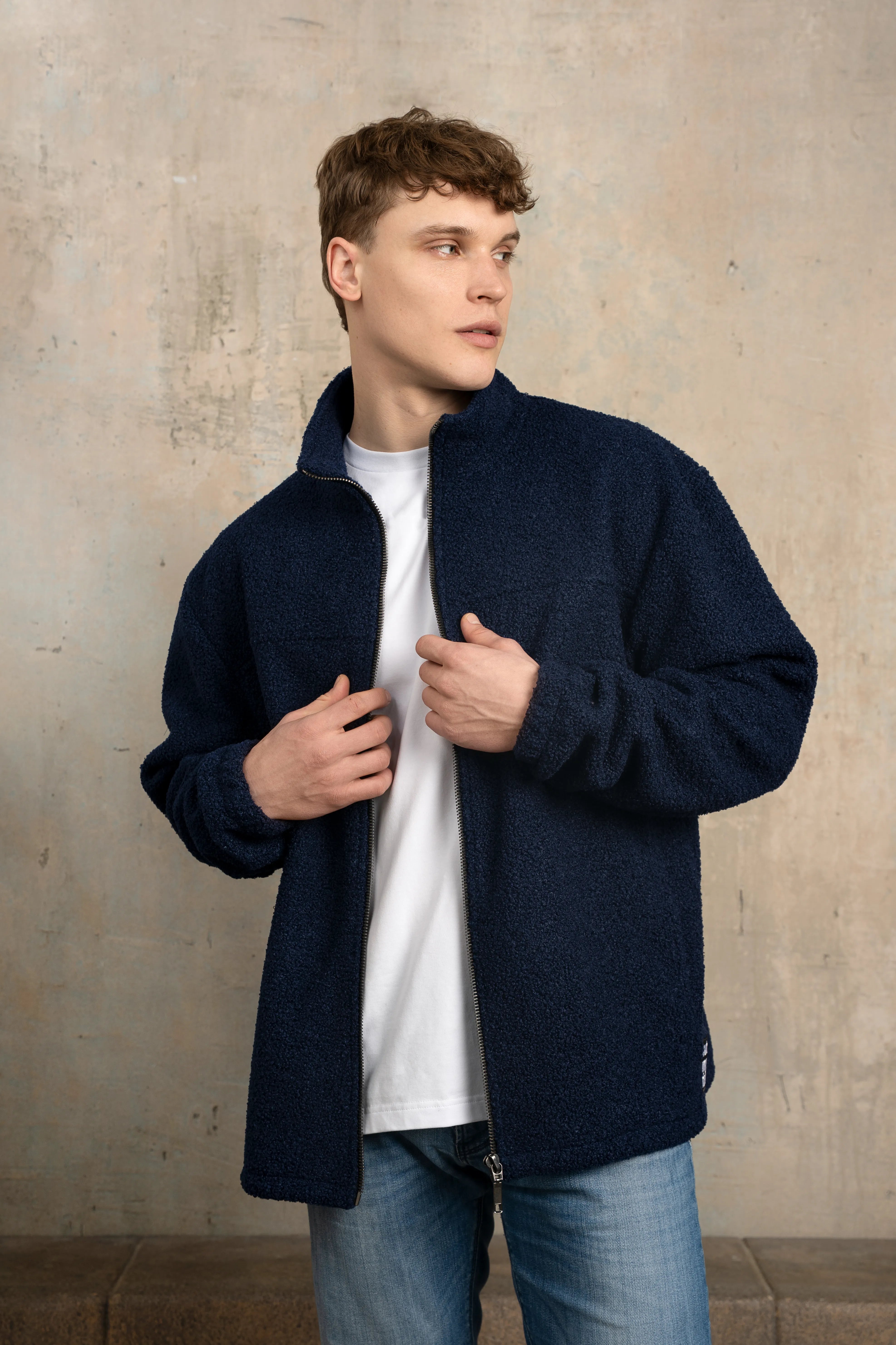 Tamsiai mėlynos spalvos vyriškas džemperis su pilno ilgio užtrauktuku, stačia apykakle, ilgomis rankovėmis ir vaizdu sėdint