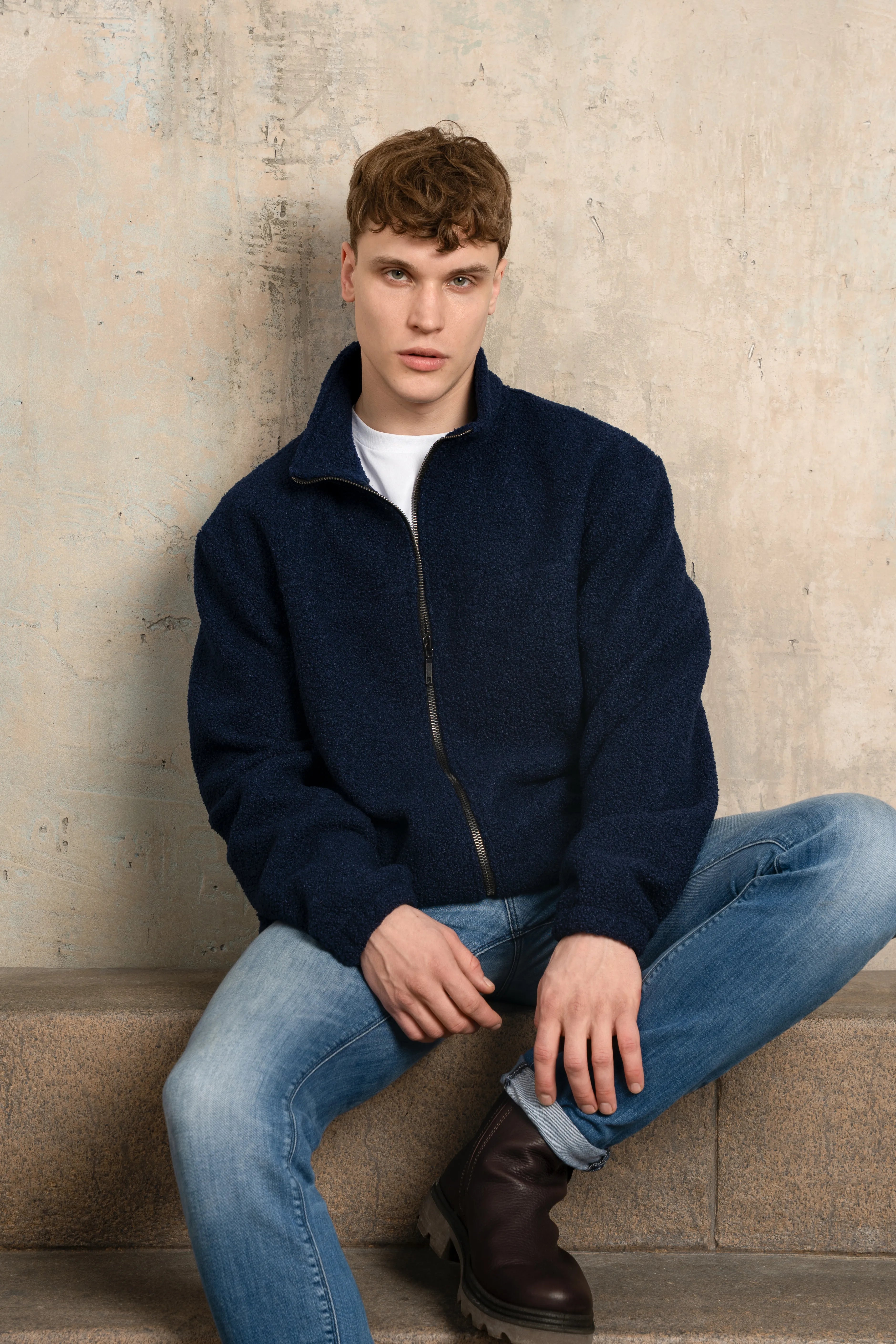 Dunkelblauer Herrenpullover mit durchgehendem Reißverschluss, Stehkragen, langen Ärmeln und lockerer Passform; das Modell wurde im Sitzen fotografiert