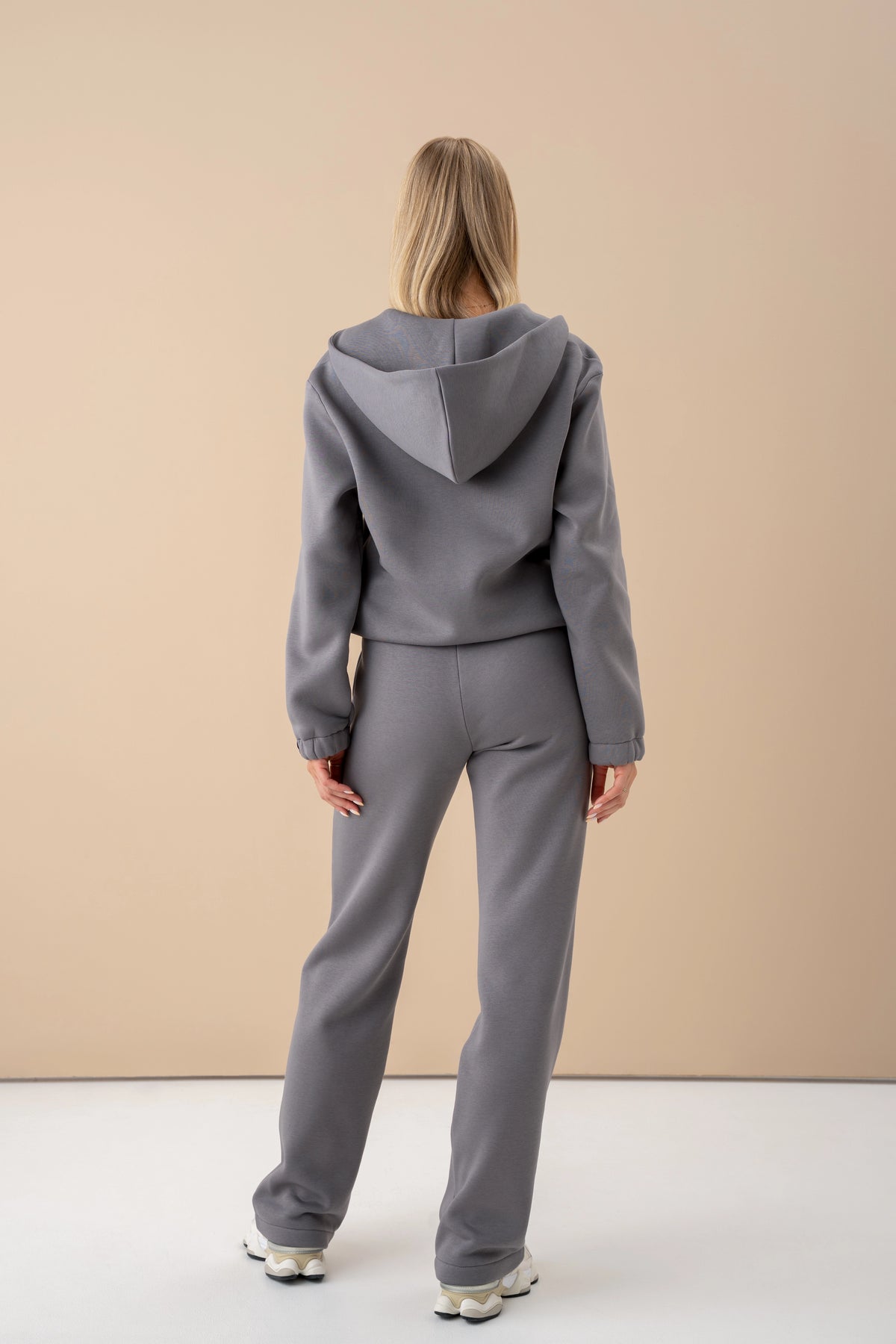 Graues Trainingsset von Cutmyfashion; das Model steht mit dem Rücken zur Kamera und trägt weiße Sportschuhe