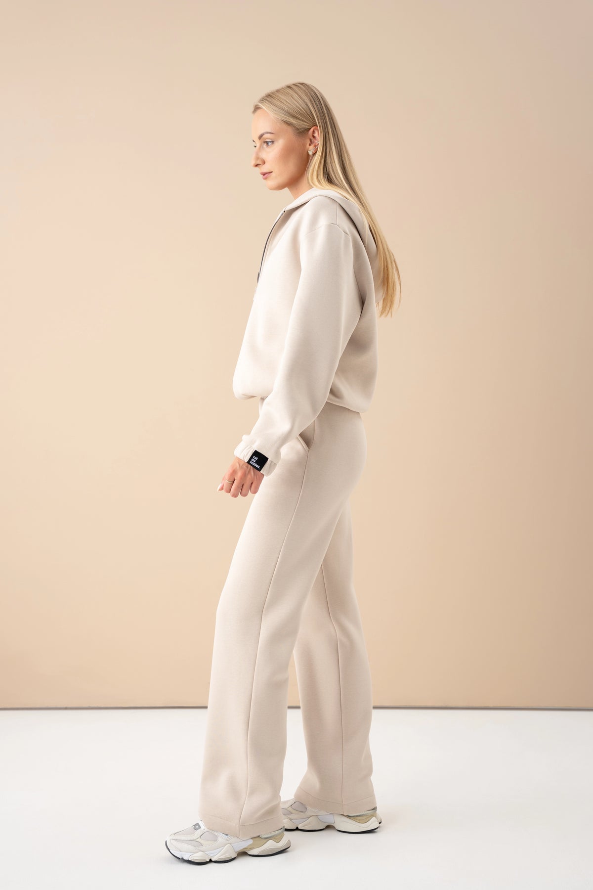 Eine Frau trägt einen Oversize-Pullover und eine Hose und geht durch ein Studio; Seitenansicht