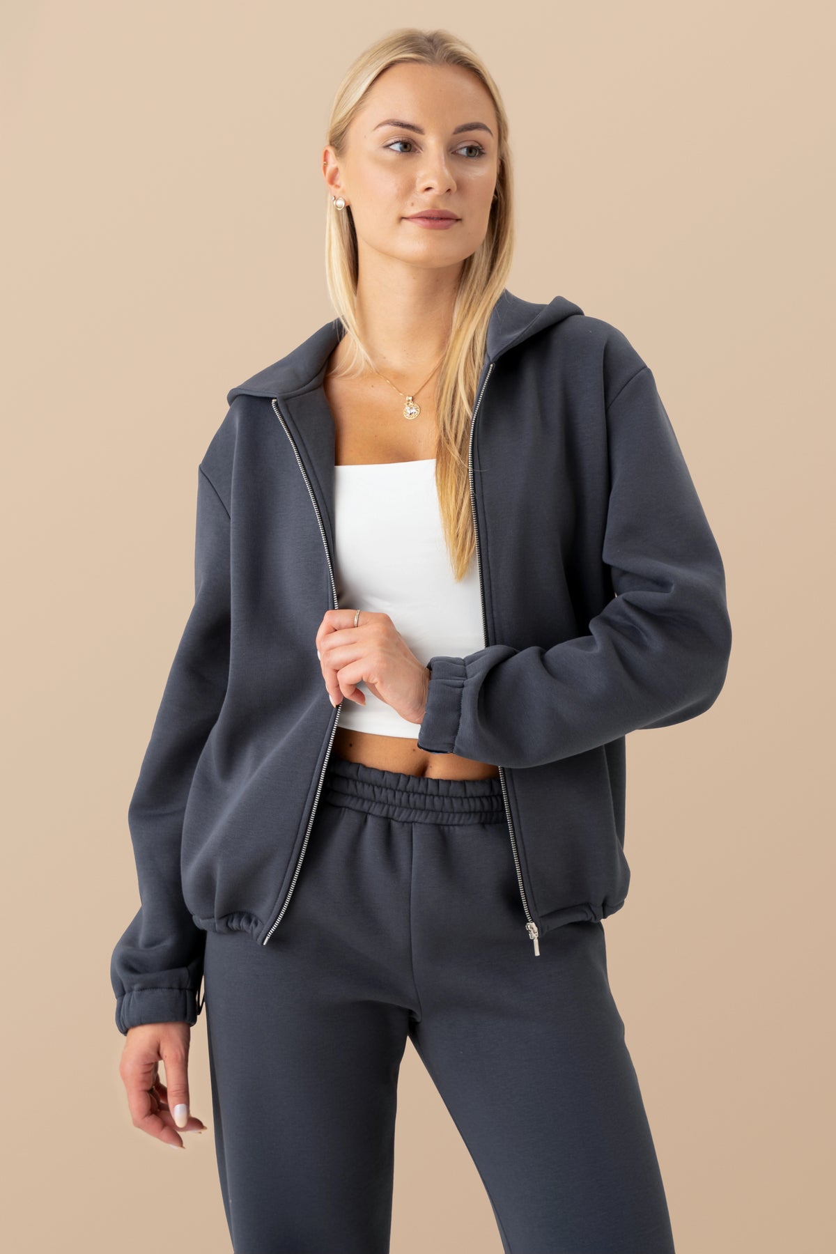 Ein Model mit einem dunkelgrauen Cutmyfashion-Pullover und einer weißen Bluse vor einem hellen Studiohintergrund