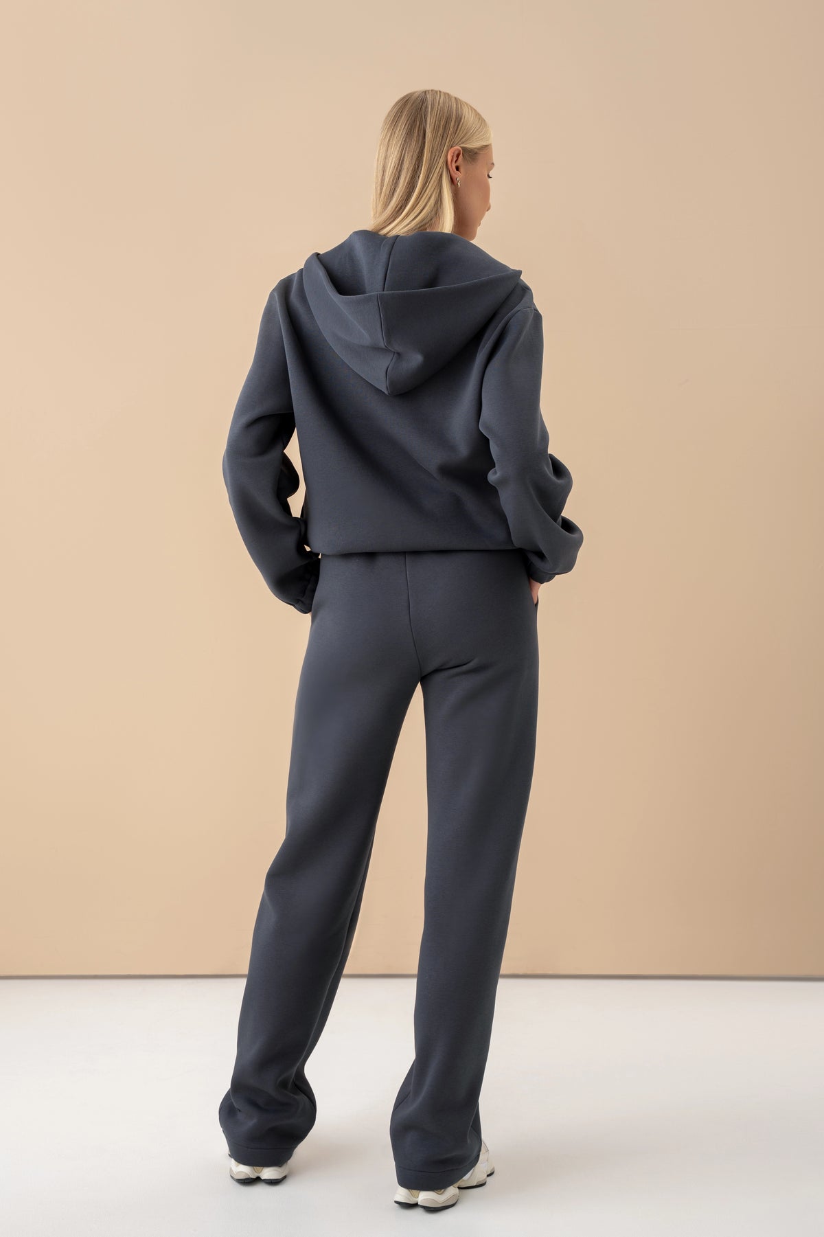 Eine Frau in einem eisblauen Pullover und einer Hose steht mit dem Rücken zur Kamera und trägt weiße Sportschuhe