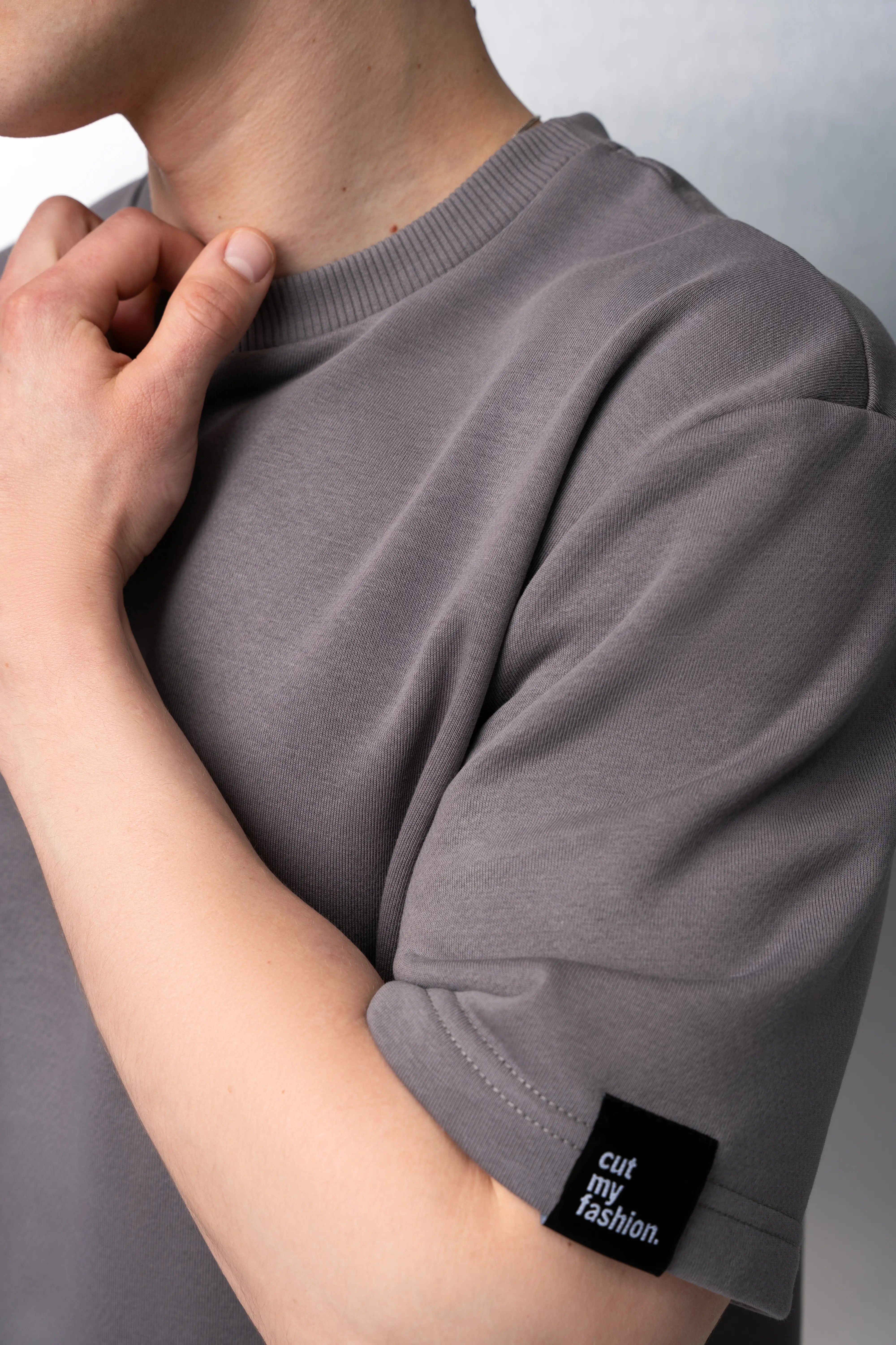 Graues Oversize-T-Shirt für Herren aus flauschfreiem Stoff, mit kurzen Ärmeln, Rundhalsausschnitt und schwarzem „cutmyfashion“-Logo auf dem Ärmel.